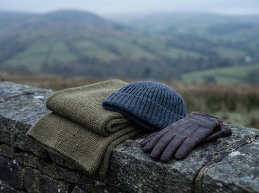 Olive wool scarf, navy knit beanie and leather gloves on a dry stone wall in the hills
