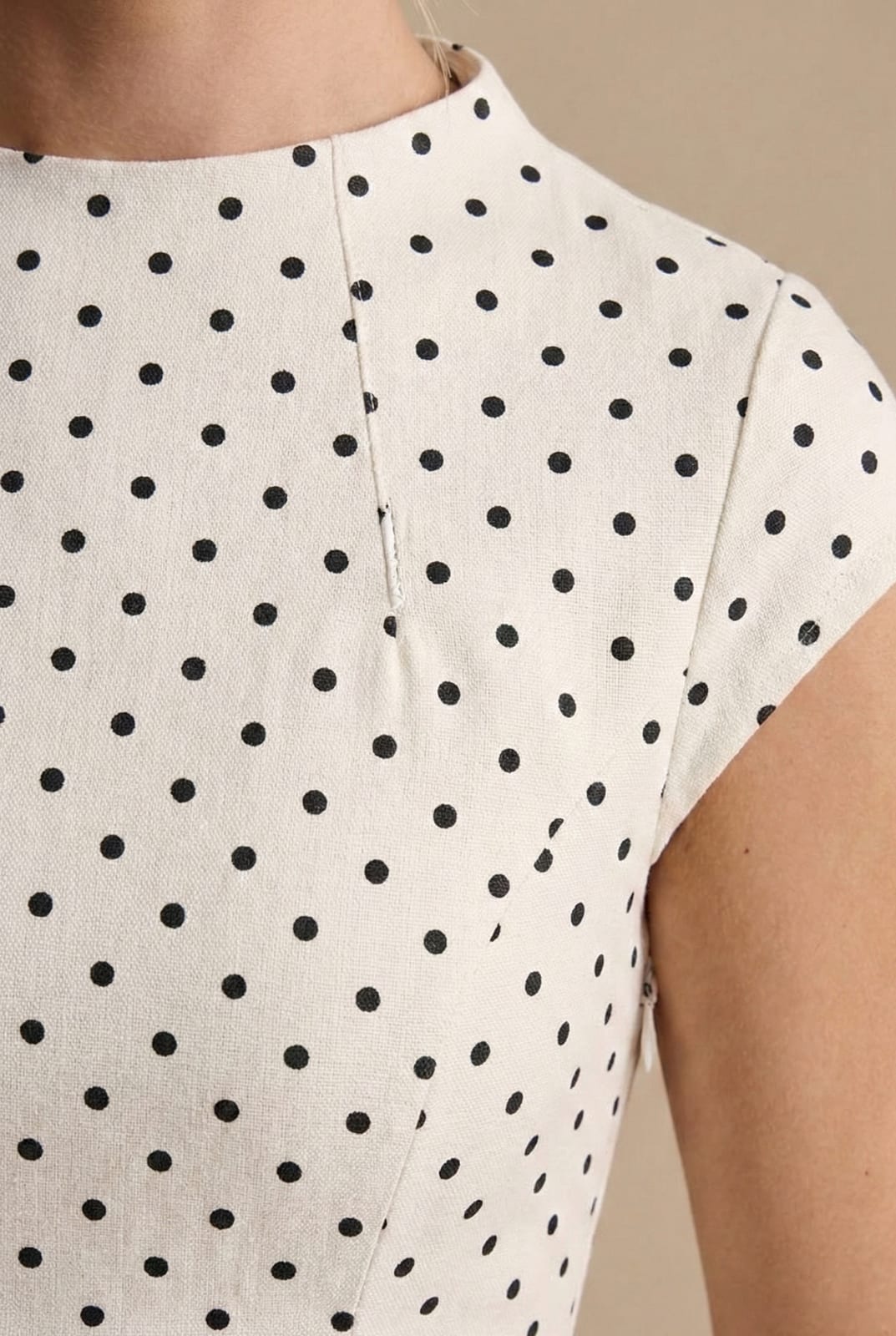 Close up of the high round neckline and cap sleeve with black dots on ivory